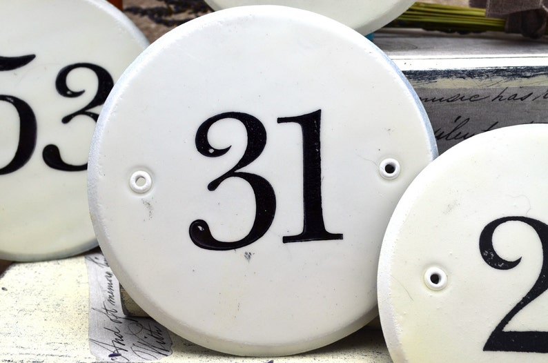 May include: Three white ceramic house number plaques with black numbers. The numbers are 53, 31, and 2. The plaques have a small hole on each side.