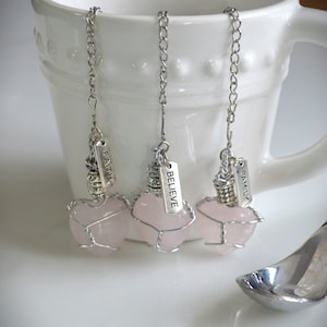 May include: Three pink heart-shaped tea infusers with silver chains and tags that read "Faith", "Believe", and "Family".