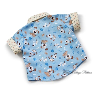 May include: A light blue short-sleeved shirt with a pattern of brown and white cartoon dogs and blue paw prints. The shirt has a white collar with a yellow and red trim. The text "arf" and "bark!" is repeated throughout the pattern.