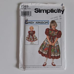 Può includere: Una busta per cartamodello Simplicity, numero 7349, taglia AA 3, 4, 5, 6. Il fronte presenta un'illustrazione Daisy Kingdom di un vestito con corpetto rosso scuro, maniche a sbuffo e gonna fantasia, insieme a un design per vestito da bambola.