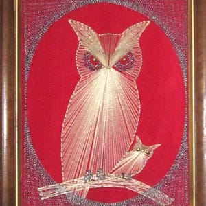 May include: Framed artwork featuring an owl and owlet design. The artwork is created with gold and silver thread on a red background. The frame is a dark brown color. The owl is perched on a branch.
