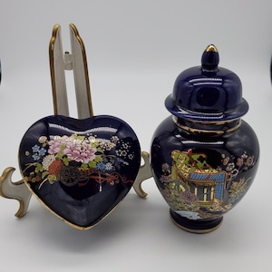 May include: A set of two blue and gold ceramic decorative pieces. One piece is a heart-shaped trinket box with floral designs. The other piece is a round jar with a lid and floral and geometric designs.