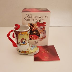 May include: A white porcelain Christmas boot with a red ribbon. The boot is decorated with a circus theme and features a clown, elephants, and other circus performers. The boot is part of a 2002 Christmas collection.