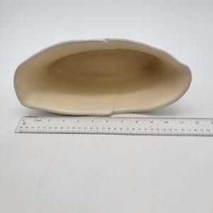 Puede incluir: Una fuente de cer&aacute;mica de color crema con un borde gris claro. La fuente mide aproximadamente 30 cm de largo y tiene una forma ovalada poco profunda. Se coloca una regla junto a la fuente para la escala.