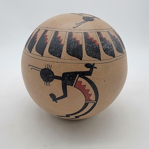 May include: A spherical tan pottery vessel featuring black and red painted designs. The upper section displays a repeating geometric pattern, while the main body showcases a stylized black figure with a curved back and red accents.