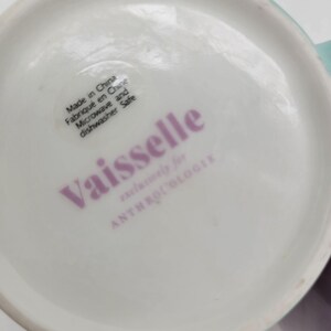 May include: White ceramic mug with the word "Vaisselle" in pink lettering. The mug has a sticker that says "Made in China, Microwave and dishwasher safe."