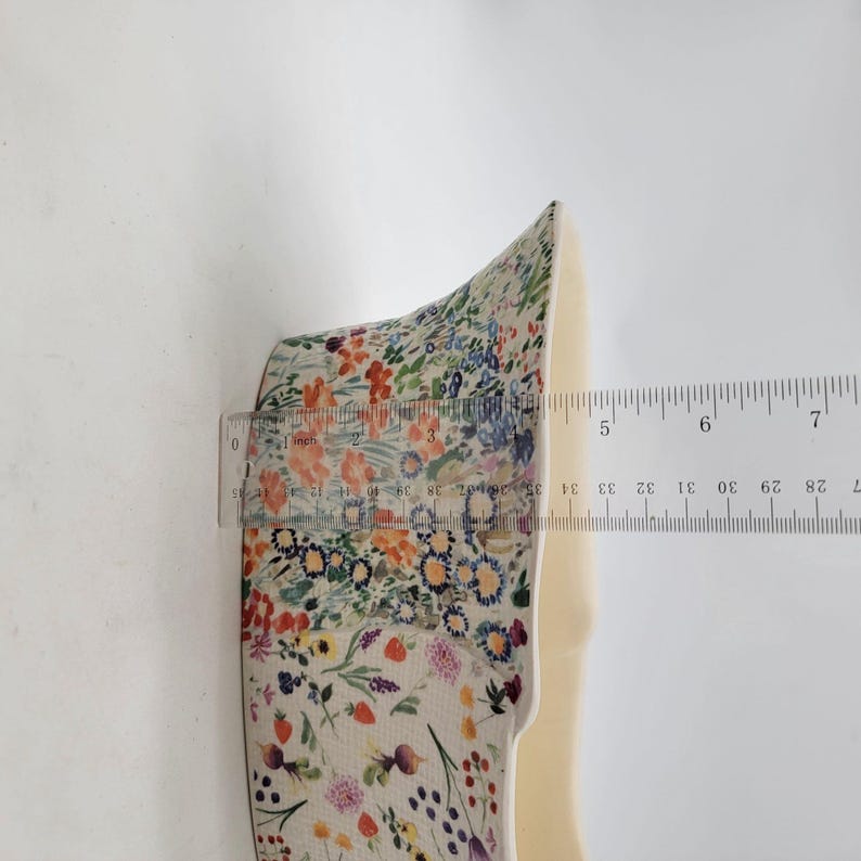 Puede incluir: Objeto con estampado floral con una regla que muestra una medida de aproximadamente 13 cm. El objeto tiene un interior color crema y est&aacute; decorado con una colorida variedad de flores y follaje.