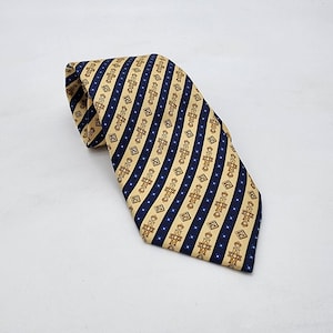 May include: A patterned tie with a beige background, navy blue stripes, and brown cross-like designs. The tie is folded and lies on a white surface. The diagonal stripes create a visually appealing pattern.