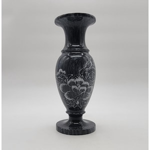 May include: A dark gray and black marble vase with a polished finish, featuring a flared rim, a slender neck, and a rounded body. The surface is etched with a white line drawing of a bird perched on a branch above a large blooming flower.