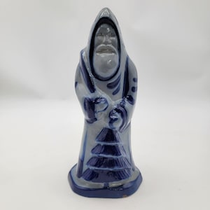 Könnte beinhalten: Keramikfigur einer vermummten Figur in Blau- und Grautönen. Die Figur hat einen langen weißen Bart und hält einen stilisierten Weihnachtsbaum. Der Sockel ist dunkelblau.