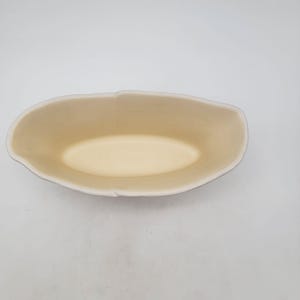 Puede incluir: Un cuenco ovalado de cer&aacute;mica con interior crema y borde blanco. El cuenco tiene un acabado liso y mate y est&aacute; vac&iacute;o. El exterior del cuenco es de color beige claro.