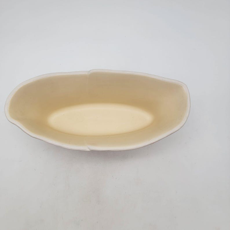 Puede incluir: Un cuenco ovalado de cer&aacute;mica con interior crema y borde blanco. El cuenco tiene un acabado liso y mate y est&aacute; vac&iacute;o. El exterior del cuenco es de color beige claro.