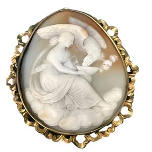 Può includere: Una spilla cammeo ovale con un rilievo bianco scolpito di una figura seduta che tiene una ciotola con un'aquila appollaiata sopra, su uno sfondo beige. Il pezzo è incastonato in una cornice di metallo dorato ornata, smerlata e traforata.