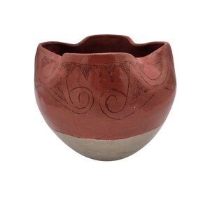 May include: A handmade terracotta-colored ceramic bowl with a cream-colored base. The bowl features etched tribal-style designs around the rim. The bowl has a unique, wavy rim and is suitable for decorative use.