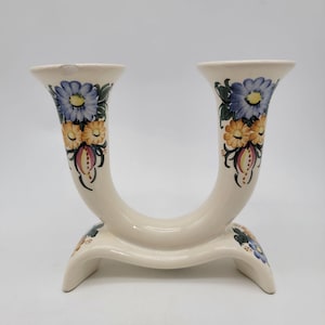 May include: Cream-colored ceramic vase with a U-shaped design. The vase features hand-painted floral patterns in blue, yellow, and pink. The vase has two openings and a curved base, suitable for displaying flowers or as a decorative piece.