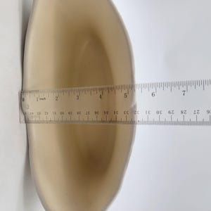 Puede incluir: Un objeto beige y curvado con una regla colocada encima. La regla muestra medidas en cent&iacute;metros, con el objeto midiendo aproximadamente 12,7 cm de largo. El objeto tiene una superficie lisa y brillante.