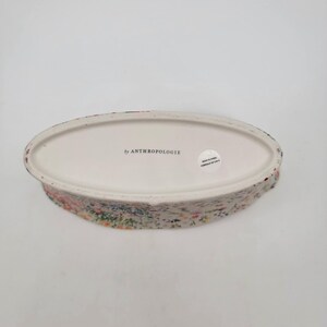 Puede incluir: Un plato de cer&aacute;mica ovalado con un estampado floral. El plato tiene un interior blanco y un exterior texturizado con un dise&ntilde;o floral colorido. Las palabras "by ANTHROPOLOGIE" est&aacute;n impresas en la parte inferior.