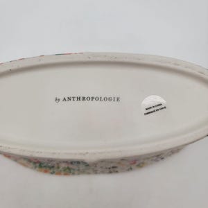 Puede incluir: Un plato ovalado de cer&aacute;mica blanca con un estampado floral en el borde. La base del plato tiene el texto "by ANTHROPOLOGIE" y una pegatina que dice "MADE IN CHINA / FABRIQU&Eacute; EN CHINE".