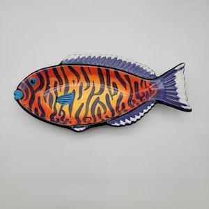 Könnte beinhalten: Eine fischförmige Servierschale aus Keramik mit einem leuchtend orange-gelben Körper und dunkelblauen vertikalen Streifen. Die Flossen und der Schwanz sind in tiefem Blau mit weißen Akzenten bemalt, das Auge ist ein hellblauer Kreis am Kopf.