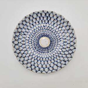 Peut inclure: Une assiette en porcelaine blanche avec un motif en treillis bleu et or. L'assiette a un bord festonné et un bord doré. Le centre de l'assiette a une petite indentation circulaire blanche avec une bordure dorée.