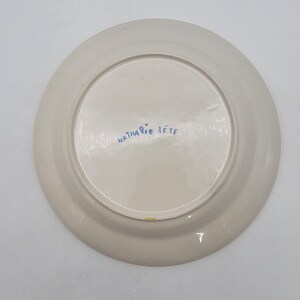 Puede incluir: Un plato de cer&aacute;mica de color crema con interior blanco. La parte inferior del plato presenta el texto manuscrito "Nathalie Lete" en azul. El plato es redondo y parece hecho a mano.