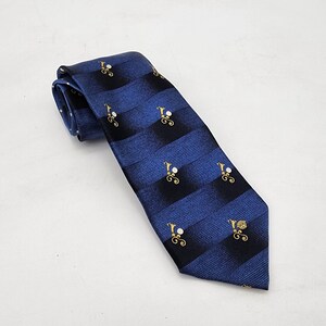 May include: A blue tie with a striped pattern and small gold and white decorative elements. The tie is folded and angled, showcasing the design. The tie is a classic accessory for formal or business attire.