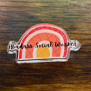 May include: A clear acrylic rainbow-shaped keychain with a red and yellow design and the text "Badass Social Worker" printed on it.