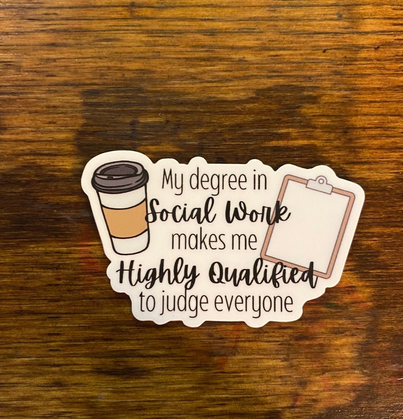 以下が含まれることがあります： コーヒーカップとクリップボードが描かれた白いステッカー。ステッカーのテキストは「ソーシャルワークの学位は、私をみんなを判断するのに非常に適任にします。」