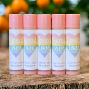 May include: Five pink lip balm tubes with white labels. The labels have a rainbow heart with the text "Thread Love" and the words "Citron and Mandarin" below.