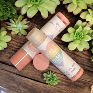 May include: Two pink lip balm tubes with rainbow hearts and the text "Spread Love" and "Citrus Flower and Jade".