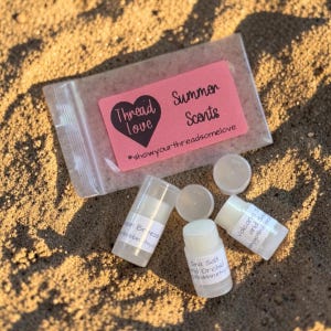 May include: A clear plastic bag with a pink label reading Thread Love Summer Scents #showyourthreadsomelove, accompanied by three small, cylindrical white lip balm tubes with labels reading Ocean Breeze, Sea Salt and Orchid, and Volcanic Sand.
