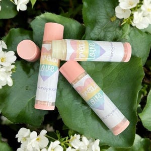 May include: Three pink lip balm tubes with rainbow hearts and the text "Spread Love" and "Honeysuckle" on them.