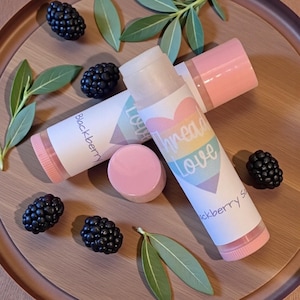 May include: Lip balm tubes with the words "Thread Love" and "Blackberry Soap" printed on them. The tubes are white with pink accents and are accompanied by black blackberries and green leaves on a wooden tray.