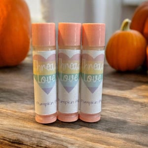 May include: Three pink lip balm tubes with labels that say "Thread Love" in a rainbow heart design. The labels also say "Pumpkin Pie" at the bottom.