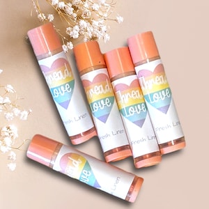 May include: Five pink lip balm tubes with rainbow heart designs and the text "Thread Love" and "Fresh Linen".