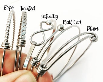 May include: Five silver bangle bracelets with different styles: rope, twisted, infinity, ball end, and plain. The bracelets are stacked on top of each other.