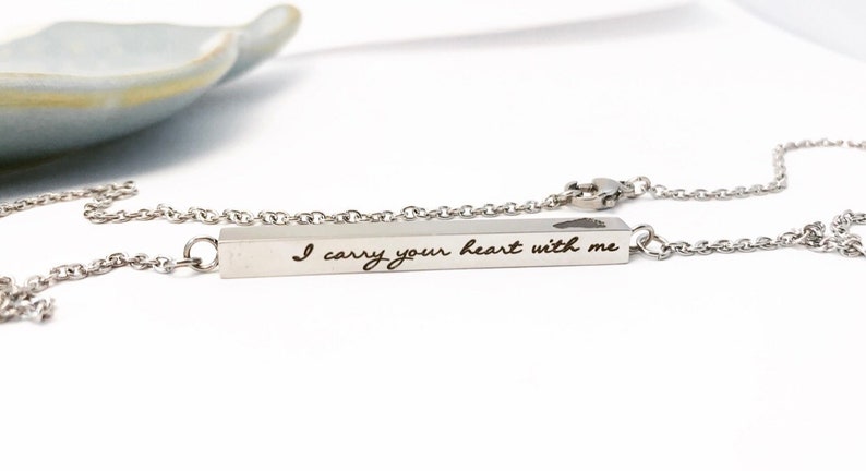 May include: Silver necklace with a bar pendant that reads "I carry your heart with me". The bar pendant has a small heart cutout.