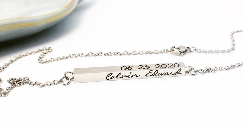 May include: A silver necklace with a bar pendant engraved with the date "06-25-2020" and the name "Calvin Edward" in cursive.