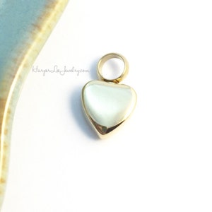 May include: A gold heart-shaped pendant with a loop at the top for attaching to a chain or bracelet.