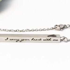 May include: A silver necklace with a bar pendant engraved with the words "I carry your heart with me" and a small footprint. The necklace is on a white background.