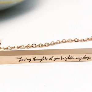 May include: A rose gold bar necklace with a chain and a bar pendant engraved with the text "Loving thoughts of you brighten my days."