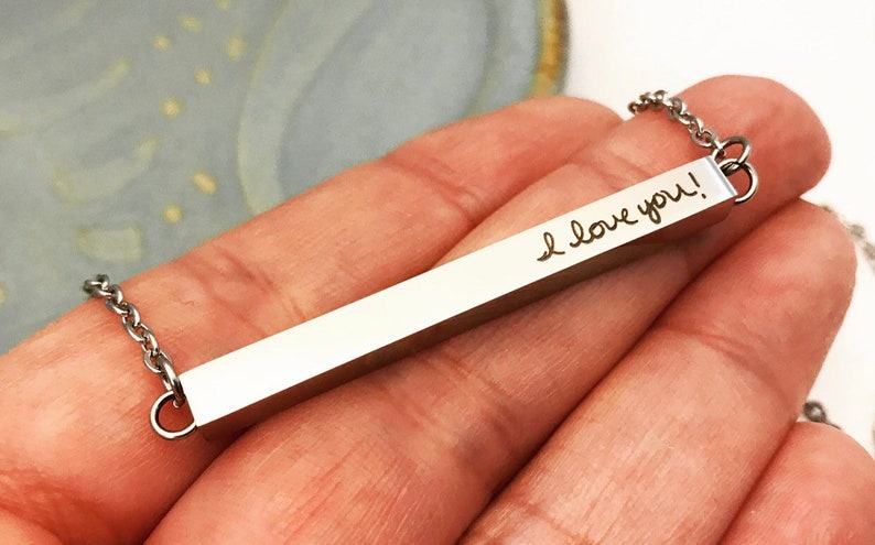 May include: A silver bar necklace with a chain. The bar is engraved with the words "I love you!" in cursive handwriting.