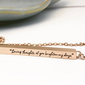 May include: A gold bar necklace with a delicate chain. The bar has the inscription "Loving thoughts of you brighten my days".