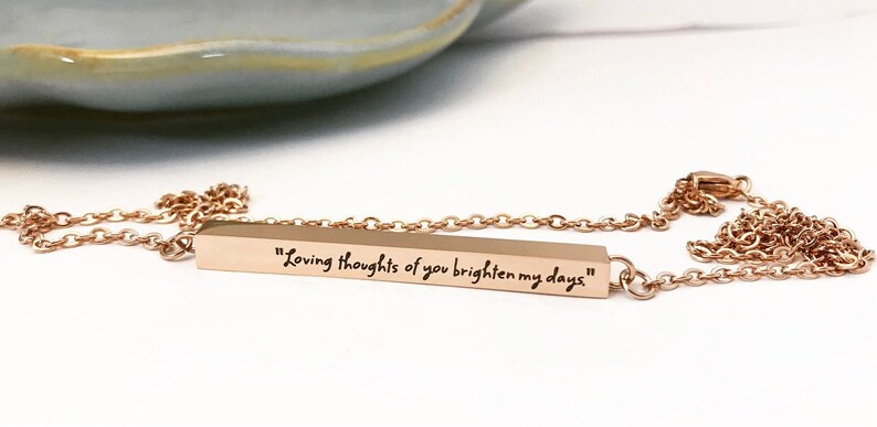 May include: A gold bar necklace with a delicate chain. The bar has the inscription "Loving thoughts of you brighten my days".