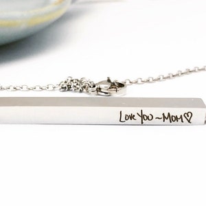 May include: A silver necklace with a bar pendant engraved with the words "Love You - Mom" and a heart symbol.