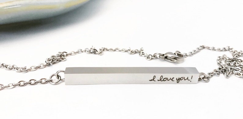 May include: A silver necklace with a bar pendant that says "I love you!" The bar pendant is attached to a silver chain.