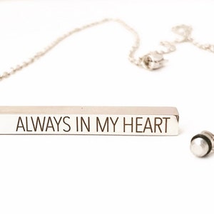 May include: A silver necklace with a bar pendant that reads "ALWAYS IN MY HEART".