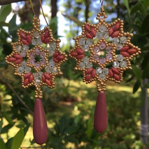 Può includere: Un paio di orecchini fatti a mano con un design a stella. Gli orecchini presentano una combinazione di perline color oro, cristalli trasparenti e perline color amaranto. Ogni orecchino ha una perla a forma di goccia color amaranto che pende dal basso.