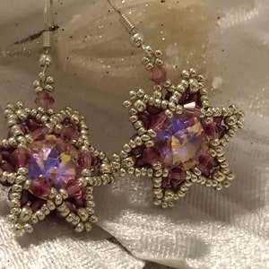 Pode incluir: Um par de brincos em forma de estrela prateados e rosados com um cristal no centro de cada estrela.