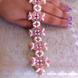 Pode incluir: Um bracelete de contas rosa e branco com detalhes dourados. O bracelete é feito de pequenas contas redondas e é enfiado em um fio.